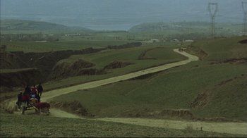 Movie still from “The Story of Qiu Ju” (1992), directed by Yimou Zhang – Two people are walking down a dirt road in a green field; Extreme Wide shot, High angle