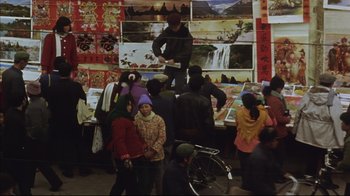 Movie still from “The Story of Qiu Ju” (1992), directed by Yimou Zhang – A group of people standing around a table with pictures on the wall; Wide shot, High angle