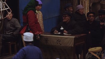Movie still from “The Story of Qiu Ju” (1992), directed by Yimou Zhang – An older man sitting at a table with a woman; Wide shot, High angle