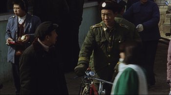 Movie still from “The Story of Qiu Ju” (1992), directed by Yimou Zhang – A man in a military uniform talking to a man on a bicycle; Medium shot, Over the shoulder angle