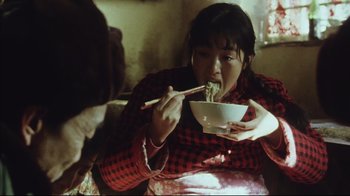 Movie still from “The Story of Qiu Ju” (1992), directed by Yimou Zhang – A woman eating a bowl of food with chopsticks; Medium shot, Low angle