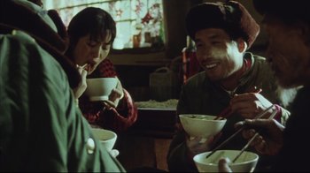 Movie still from “The Story of Qiu Ju” (1992), directed by Yimou Zhang – A man and a woman are sitting at a table with bowls of food in front of them; Medium shot, Over the shoulder angle