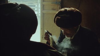 Movie still from “The Story of Qiu Ju” (1992), directed by Yimou Zhang – An older man smoking a cigarette in front of a window; Close Up shot, Over the shoulder angle