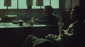 Movie still from “The Story of Qiu Ju” (1992), directed by Yimou Zhang – Two men sitting at a table in front of a cup of coffee; Medium shot, Over the shoulder angle