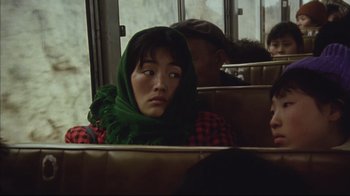 Movie still from “The Story of Qiu Ju” (1992), directed by Yimou Zhang – A woman sitting on a bus wearing a green head scarf; Close Up shot, Over the shoulder angle