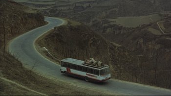 Movie still from “The Story of Qiu Ju” (1992), directed by Yimou Zhang – A bus driving down a curvy road in the mountains; Extreme Wide shot, High angle