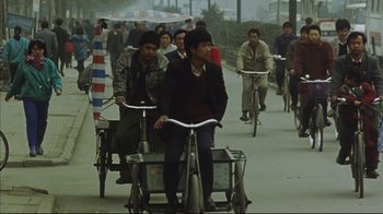 Movie still from “The Story of Qiu Ju” (1992), directed by Yimou Zhang – A group of people riding bicycles down a street; Wide shot, High angle