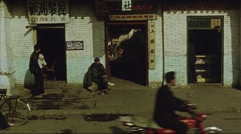 Movie still from “The Story of Qiu Ju” (1992), directed by Yimou Zhang – A man sitting on the side of the street; Wide shot, High angle