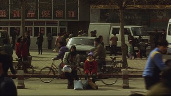 Movie still from “The Story of Qiu Ju” (1992), directed by Yimou Zhang – Two women sitting on a bench on the side of the street; Wide shot, High angle