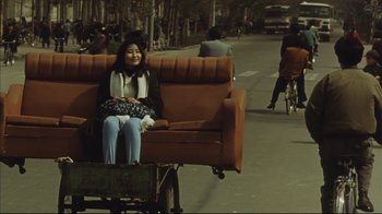 Movie still from “The Story of Qiu Ju” (1992), directed by Yimou Zhang – A woman sitting on top of a couch on the side of a road; Wide shot, High angle