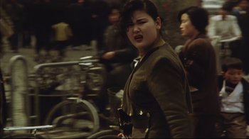 Movie still from “The Story of Qiu Ju” (1992), directed by Yimou Zhang – A woman in a brown jacket is standing in front of a bicycle; Close Up shot, Over the shoulder angle