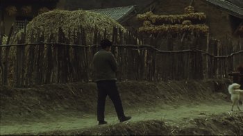 Movie still from “The Story of Qiu Ju” (1992), directed by Yimou Zhang – A man standing on a dirt road near a fence; Wide shot, High angle
