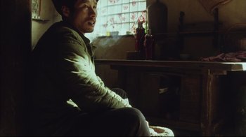 Movie still from “The Story of Qiu Ju” (1992), directed by Yimou Zhang – A man sitting in a chair in front of a window; Medium shot, High angle