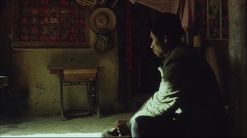 Movie still from “The Story of Qiu Ju” (1992), directed by Yimou Zhang – A man sitting on a chair in a room; Medium shot, Over the shoulder angle