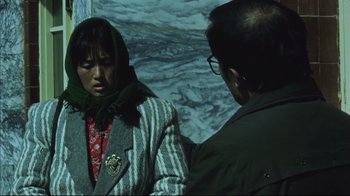Movie still from “The Story of Qiu Ju” (1992), directed by Yimou Zhang – A man and a woman are standing in front of a wall; Medium shot, High angle