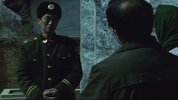 Movie still from “The Story of Qiu Ju” (1992), directed by Yimou Zhang – A man in a uniform looking at himself in a mirror; Medium shot, Over the shoulder angle