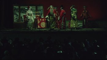 Movie still from “The Story of Qiu Ju” (1992), directed by Yimou Zhang – A group of people sitting on a stage; Wide shot, High angle
