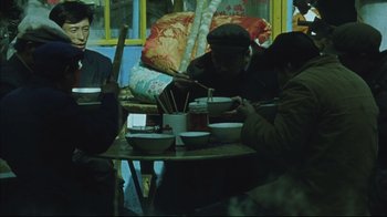 Movie still from “The Story of Qiu Ju” (1992), directed by Yimou Zhang – A group of people sitting at a table with bowls of food; Medium shot, High angle