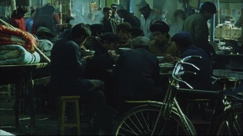 Movie still from “The Story of Qiu Ju” (1992), directed by Yimou Zhang – A group of people sitting at a table eating food; Wide shot, High angle