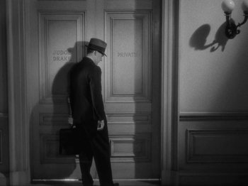 Movie still from “The Story of Temple Drake” (1933), directed by Stephen Roberts – A black and white photo of a man in a suit and hat; Wide shot, High angle