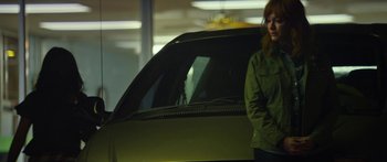Movie still from “The Strangers: Prey at Night” (2018), directed by Johannes Roberts – A woman standing in front of a car in a parking lot; Medium shot, Over the shoulder angle