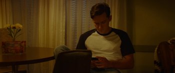Movie still from “The Strangers: Prey at Night” (2018), directed by Johannes Roberts – A man sitting on a chair looking at his cell phone; Medium shot, High angle