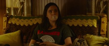 Movie still from “The Strangers: Prey at Night” (2018), directed by Johannes Roberts – A woman sitting on a couch with a chewing gum bubble in her mouth; Medium shot, Over the shoulder angle