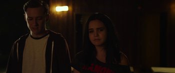 Movie still from “The Strangers: Prey at Night” (2018), directed by Johannes Roberts – A woman standing in a dark room looking sad; Medium shot, Over the shoulder angle