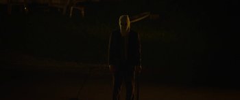 Movie still from “The Strangers: Prey at Night” (2018), directed by Johannes Roberts – A man in a suit and a mask standing in the dark; Medium shot, High angle