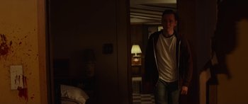 Movie still from “The Strangers: Prey at Night” (2018), directed by Johannes Roberts – A man standing in a room with a lamp on the wall behind him; Medium shot, Over the shoulder angle