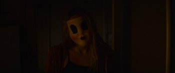 Movie still from “The Strangers: Prey at Night” (2018), directed by Johannes Roberts – A woman wearing a mask in a dark room; Close Up shot, Over the shoulder angle