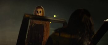 Movie still from “The Strangers: Prey at Night” (2018), directed by Johannes Roberts – A person wearing a mask and holding a gun in the dark; Medium shot, Over the shoulder angle