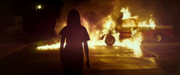 Movie still from “The Strangers: Prey at Night” (2018), directed by Johannes Roberts – A woman standing in front of a burning car; Wide shot, Low angle