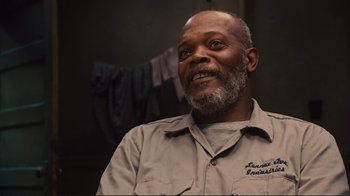 Movie still from “The Sunset Limited” (2011), directed by Tommy Lee Jones – An older man with a gray beard is smiling for the camera; Close Up shot, Over the shoulder angle