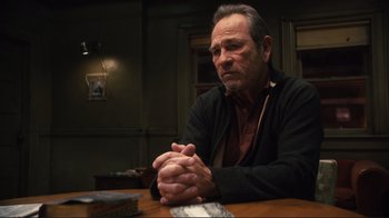 Movie still from “The Sunset Limited” (2011), directed by Tommy Lee Jones – An older man sitting at a table with his hands clasped together; Medium shot, Over the shoulder angle