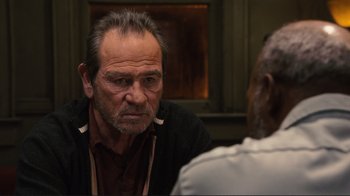 Movie still from “The Sunset Limited” (2011), directed by Tommy Lee Jones – A man sitting in front of another man in front of a window; Close Up shot, Over the shoulder angle