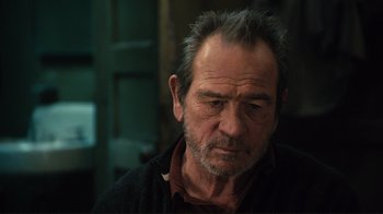 Movie still from “The Sunset Limited” (2011), directed by Tommy Lee Jones – An older man with a gray beard looking at the camera; Close Up shot, Over the shoulder angle