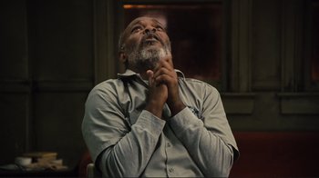Movie still from “The Sunset Limited” (2011), directed by Tommy Lee Jones – An older man with a gray beard is praying; Medium shot, Low angle