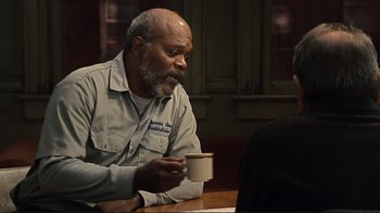 Movie still from “The Sunset Limited” (2011), directed by Tommy Lee Jones – An older man sitting at a table with a cup of coffee; Medium shot, Over the shoulder angle
