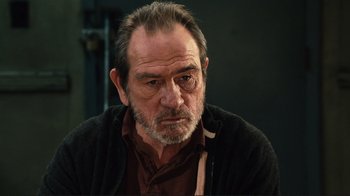 Movie still from “The Sunset Limited” (2011), directed by Tommy Lee Jones – An older man with a beard and mustache wearing glasses; Close Up shot, Over the shoulder angle