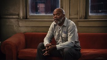 Movie still from “The Sunset Limited” (2011), directed by Tommy Lee Jones – An older man sitting on a red couch in front of a window; Medium shot, Low angle