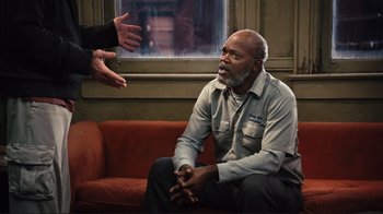 Movie still from “The Sunset Limited” (2011), directed by Tommy Lee Jones – An older man sitting on a couch talking to someone; Medium shot, Over the shoulder angle