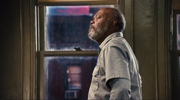 Movie still from “The Sunset Limited” (2011), directed by Tommy Lee Jones – An older man standing in front of a window; Medium shot, Low angle