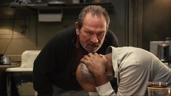 Movie still from “The Sunset Limited” (2011), directed by Tommy Lee Jones – An older man with a beard is holding his hands across his chest while a younger man holds his hands across his chest; Close Up shot, Over the shoulder angle