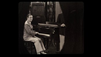 Movie still from “The Sunshine Boys” (1975), directed by Herbert Ross – A man sitting at a piano in front of another man in a suit; Medium shot, High angle