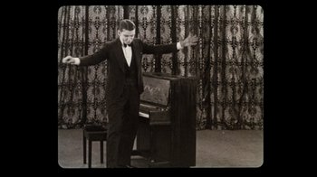 Movie still from “The Sunshine Boys” (1975), directed by Herbert Ross – A black and white photo of a man standing next to a piano; Medium shot, High angle