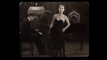 Movie still from “The Sunshine Boys” (1975), directed by Herbert Ross – A woman in a black dress standing in front of a piano; Medium shot, Low angle