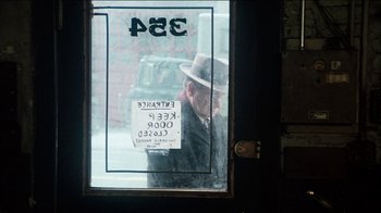Movie still from “The Sunshine Boys” (1975), directed by Herbert Ross – A man in a hat is looking out of a store window; Wide shot, Over the shoulder angle