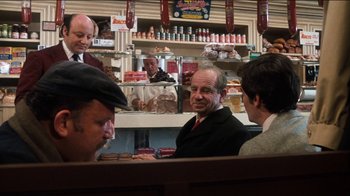 Movie still from “The Sunshine Boys” (1975), directed by Herbert Ross – A group of people sitting at a table in front of a counter; Medium shot, Over the shoulder angle