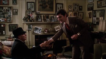 Movie still from “The Sunshine Boys” (1975), directed by Herbert Ross – A man and woman shaking hands in front of a fireplace; Medium shot, Over the shoulder angle
